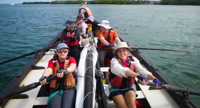 a group of people wearing life jackets use oars to navigate a sailing boat